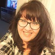 Kim Baccellia author image 2026 with plaid shirt, glasses, dark hair and a smile