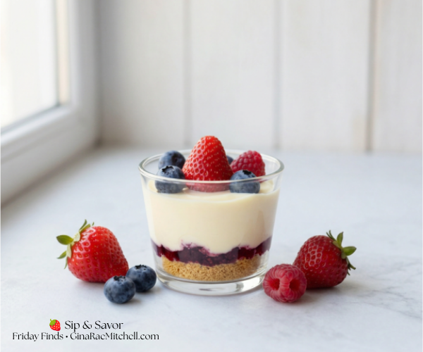 A clear glass cup of no-bake berry cheesecake on a light counter in front of a window