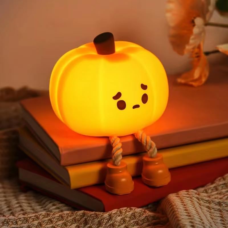 Glowing orange pumpkin nightlight with a cute face, dangling rope legs, and little brown boots, sitting on a stack of books.