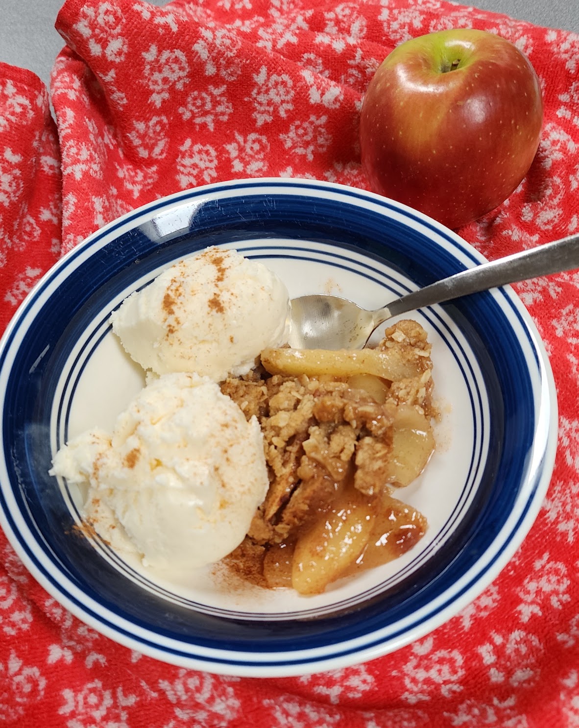 Homemade apple crisp made with Cosmic Crisp and Honeycrisp apples, served with vanilla ice cream and a sprinkle of cinnamon.
